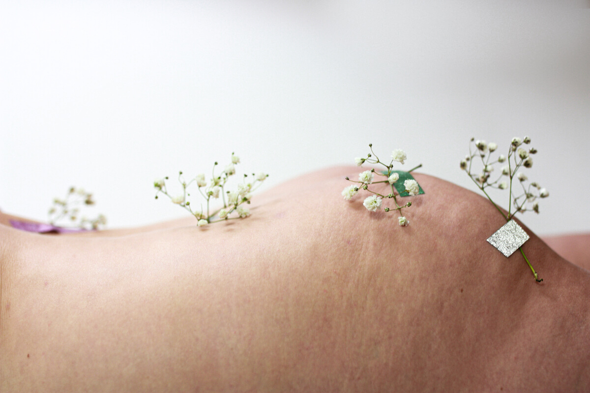 Kwiaty przyklejone na ciele nagiej kobiety.