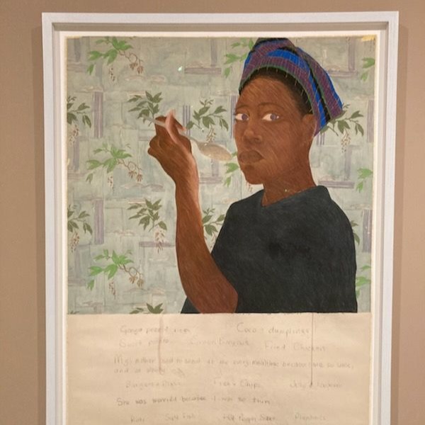 Reprodukcja obrazu Ryż z groszkiem autorstwa Sonii Boyce. Pastel na papierze z 1982 roku. Przedstawia ciemnoskórą kobietę w ciemnej bluzce i kolorowej chuście na głowie, trzymającą łyżkę uniesioną w kierunku ust. Postać ukazana jest na tle jasnej, wzorzystej tapety z motywem roślinnym. Obraz oprawiony w jasną ramę, poniżej widoczny fragment papieru z odręcznymi notatkami.