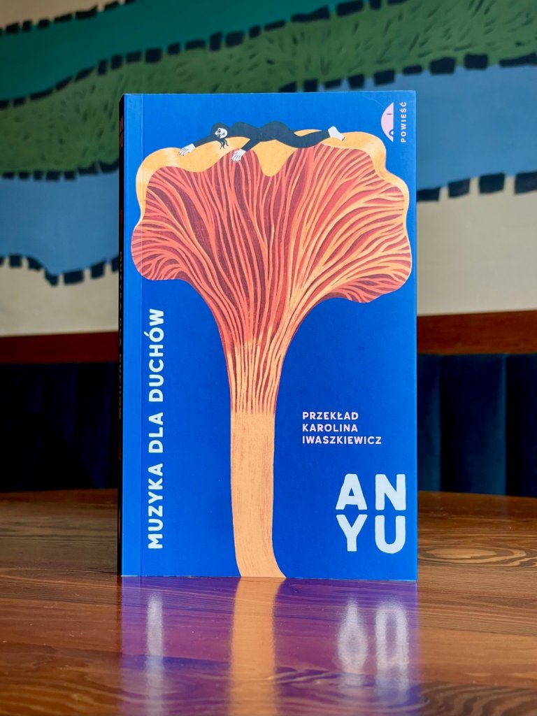 Okładka książki „Muzyka dla duchów”, autorka: An Yu, wydawnictwo Czarne; ilustracja postaci leżącej na dużym grzybie na niebieskim tle.