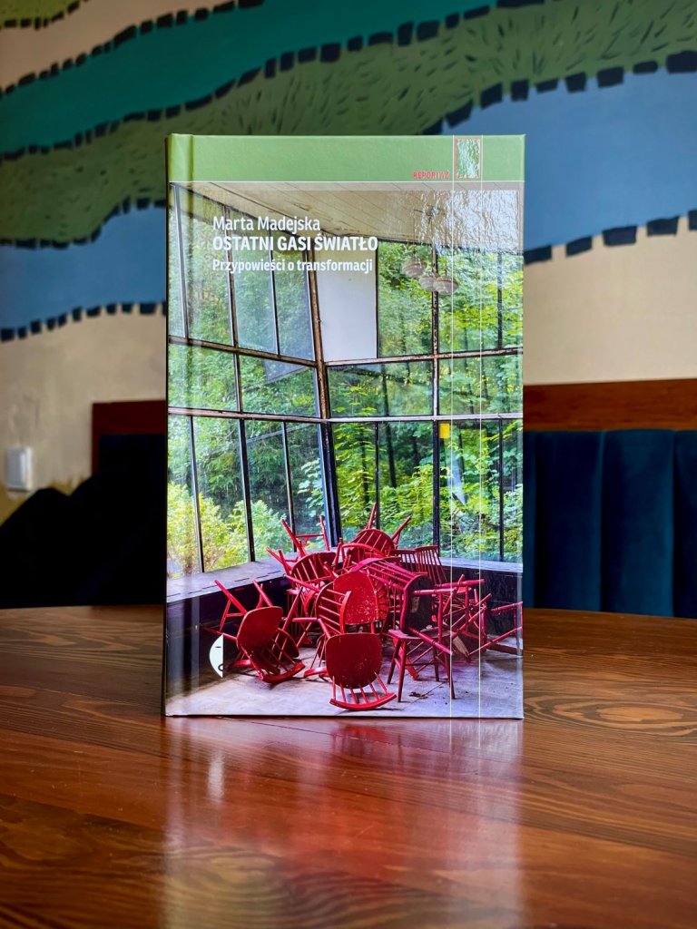 Okładka książki „Ostatni gasi światło. Przypowieści o transformacji”, autorka: Marta Madejska, wydawnictwo Czarne; zdjęcie przewróconych czerwonych krzeseł w przeszklonym wnętrzu.