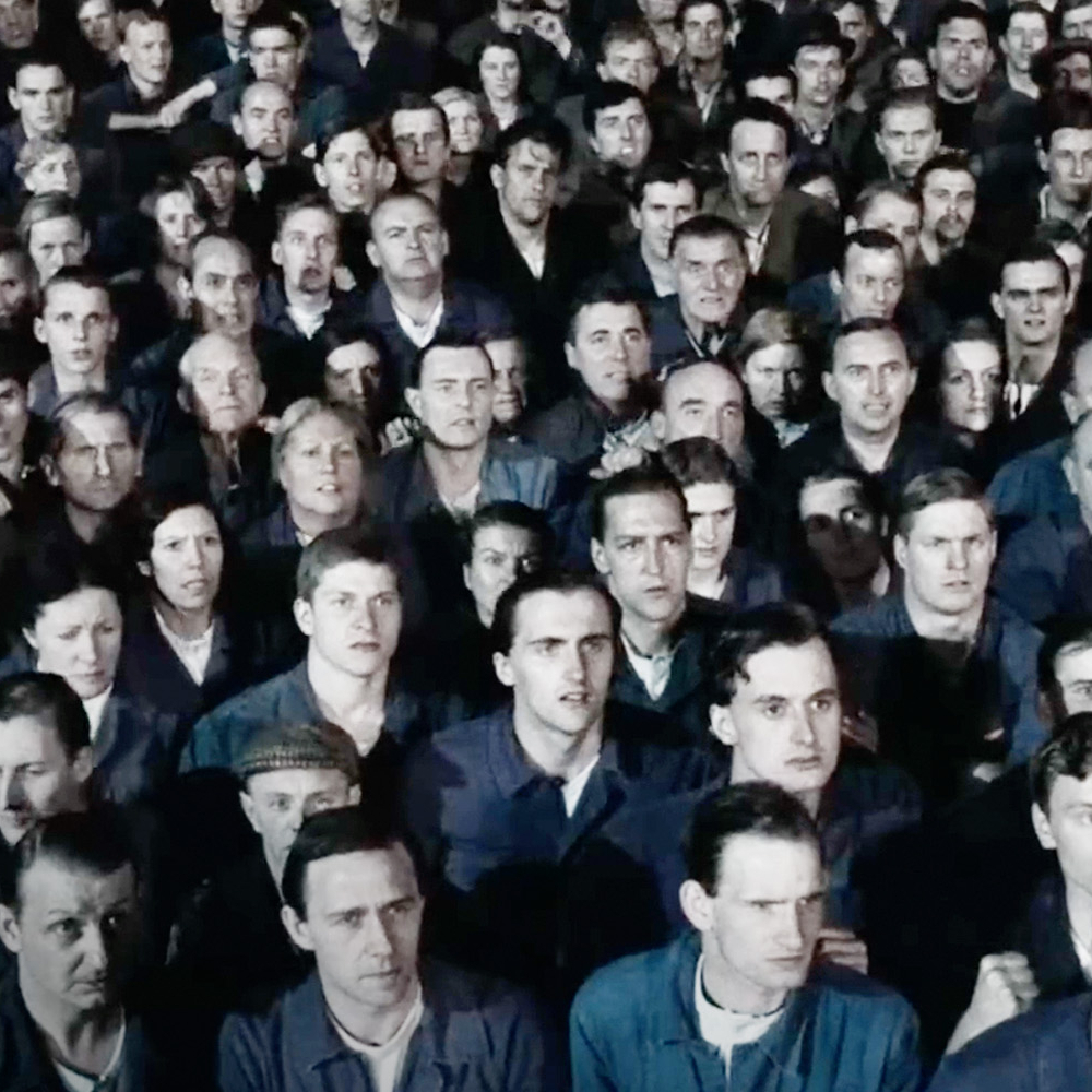 Tłum ludzi patrzy w jednym kierunku, napięte twarze i atmosfera kontroli społecznej. Film dokumentalny „Orwell 2+2=5”, reż. Raoul Peck, MDAG 2026.