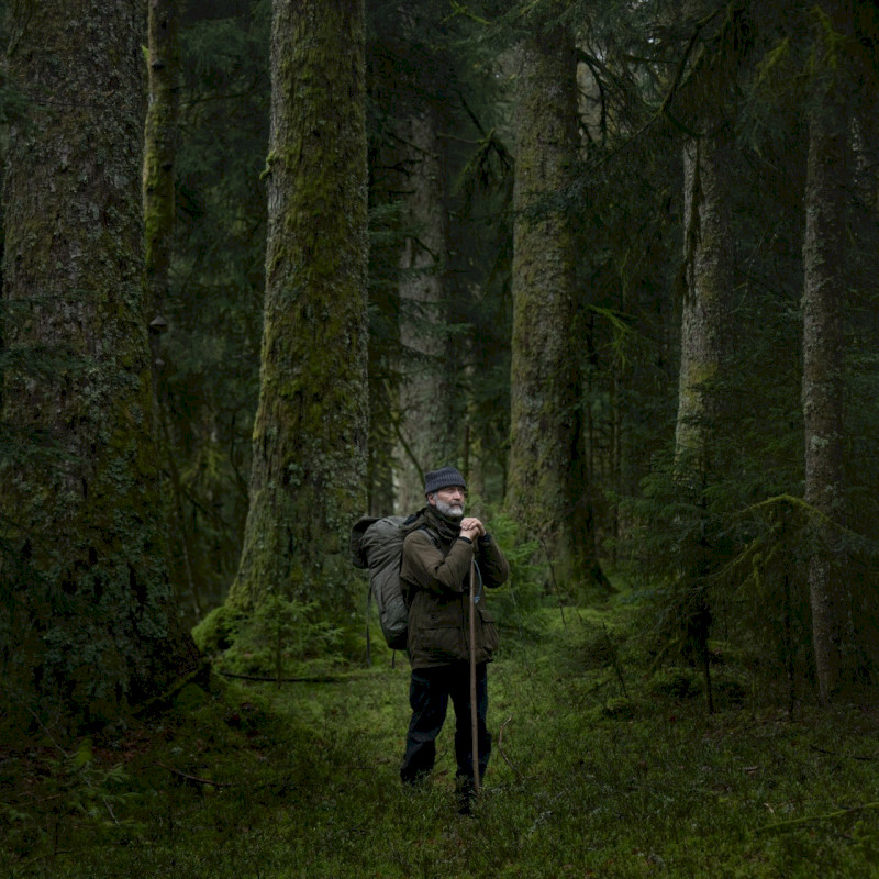 Mężczyzna z plecakiem stoi w gęstym lesie, kontempluje naturę i ciszę. Film dokumentalny „Pieśni lasu”, reż. Vincent Munier, MDAG 2026.