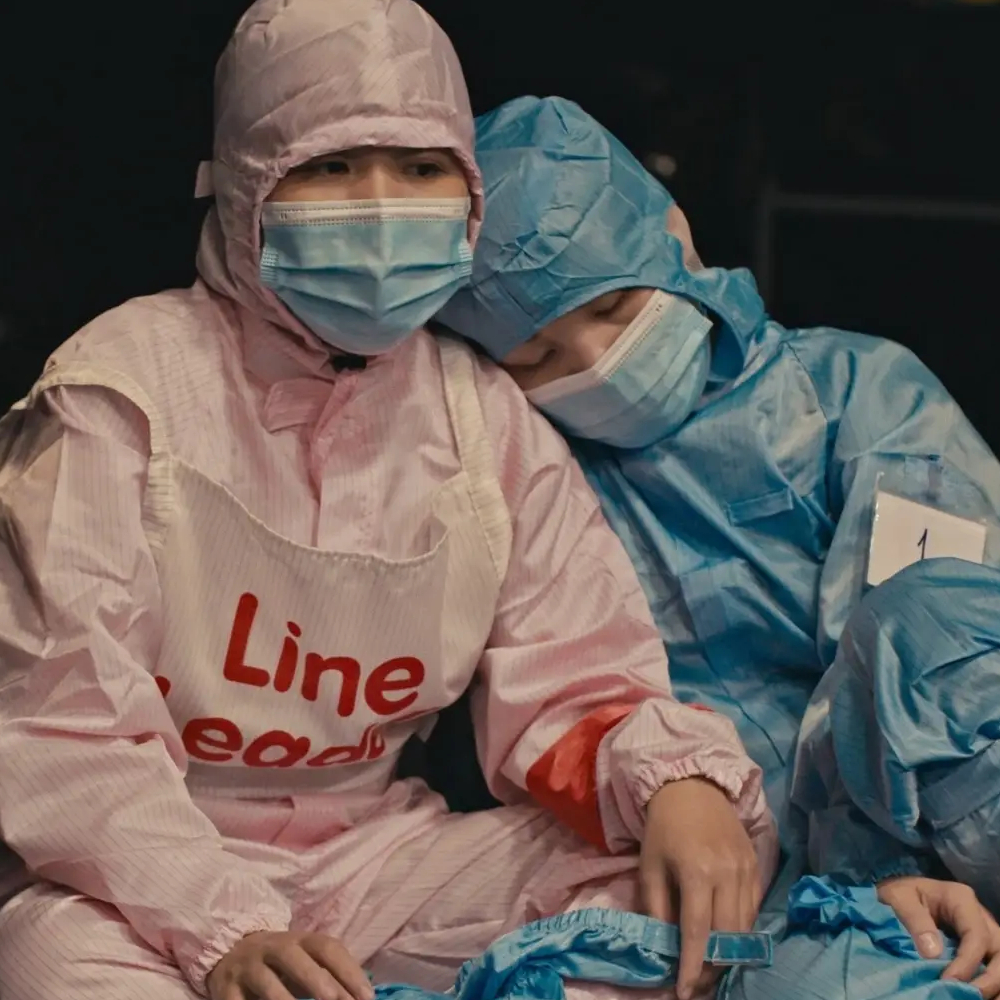 Dwie osoby w kombinezonach ochronnych siedzą blisko siebie, jedna opiera głowę na drugiej. Film dokumentalny „She”, reż. Parsifal Reparato, MDAG 2026.