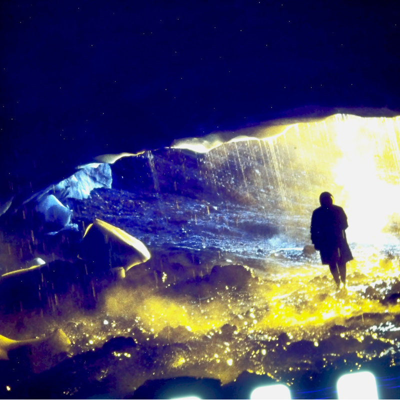 Postać stoi nocą przy wodzie oświetlonej światłem, dynamiczne fale i refleksy. Film dokumentalny „Time and Water”, reż. Andri Snær Magnason, MDAG 2026.